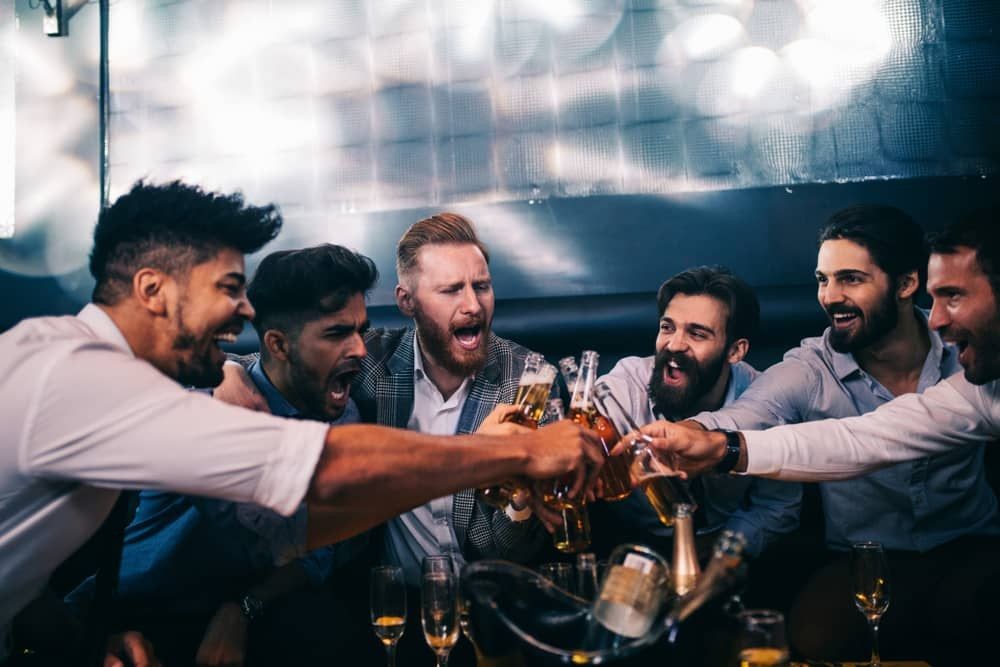 Group of friends celebrating during a Las Vegas strip club crawl, enjoying VIP access and drinks as part of a bachelor party package for California visitors.